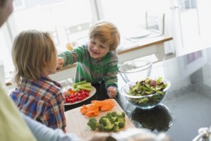 Younger brother feeding older brother a vegetable stick.