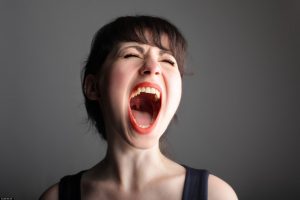 Mujer-gritando-con-la-boca-abierta-sobre-un-fondo-gris-negruzco
