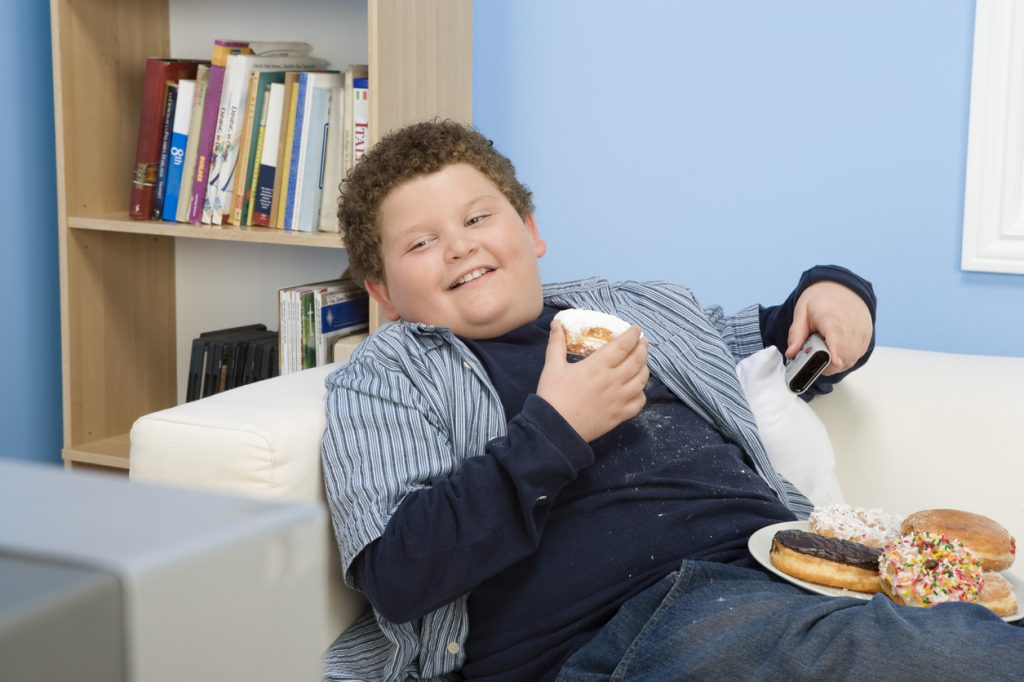 Niño con sobrepeso comiendo en el sofá