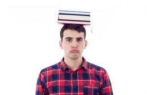 Stressed Upset student with pile of books on his head