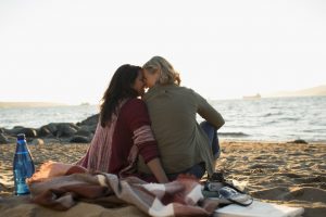 Tender, affectionate lesbian couple sitting on blanket on ocean beach
