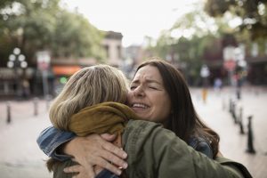 Happy mature women friends hugging on sidewalk