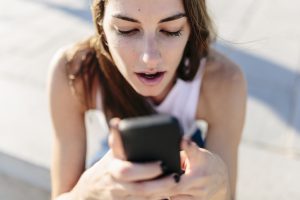 Astonished young woman looking at cell phone