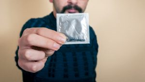 Midsection Of Man Holding Condom Packet Against Wall