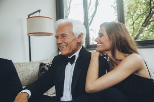 Smiling young woman with elegant senior man on couch