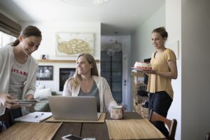 Teenage daughters surprising mother working at laptop with cake