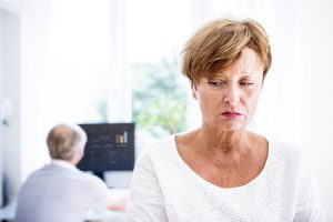 Serious senior woman with husband in background using computer