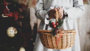 Little girl on Christmas stage holding a basket next to a Christmas tree.