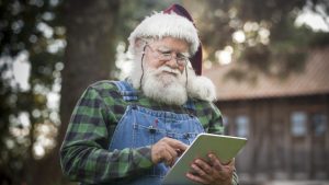 Santa Claus checking his digital tablet in front of his log cabin in the woods