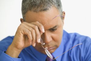 Close up of mature man holding glasses with hand on face