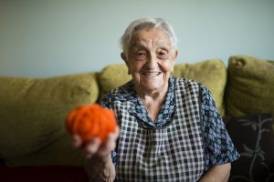 Portrait of smiling senior woman with ball of wool sitting on the couch at home