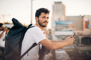 Side view portrait of young man holding mobile phone while leaning on railing at bridge