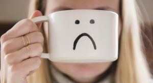 Woman holding mug with sad face in front of face