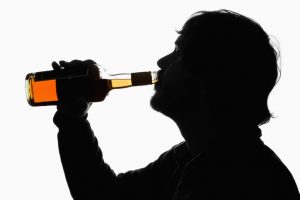 A silhouetted man drinking whiskey from the bottle