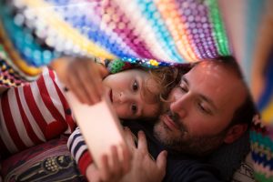 Boy and dad  watching something in a smartphone under a colorful blanket