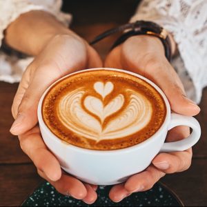 Cropped shot of woman hands holding a cup of hot latte coffee in her hands.