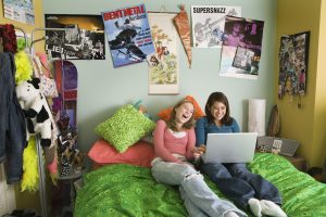 Two teenage girls (14-16) using laptop on bed, laughing