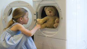 Little girl taking teddy bear out of dryer