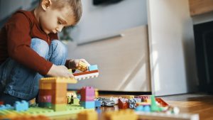 Little boy crouching on the floor at home playing with building bricks