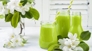 Detox, healthy green smoothie in jars and bottle. White wooden rustic background with apple blossom
