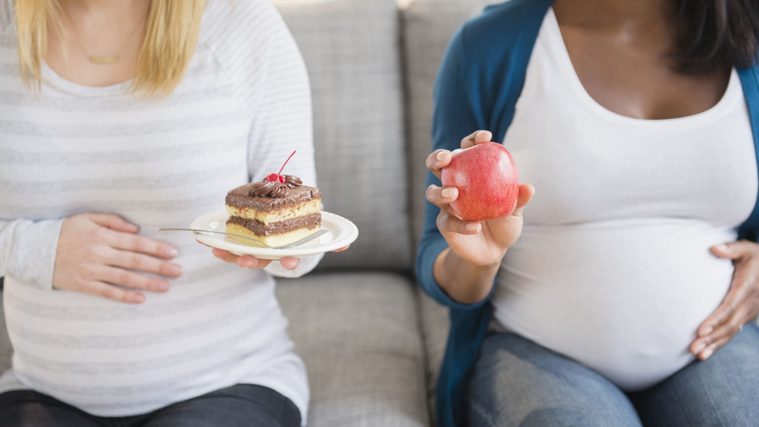 Dos madres debaten sobre los antojos durante el embarazo mostrando un dulce y una fruta.