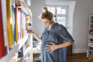 Una mujer embarazada organiza la estantería de libros de su hogar.