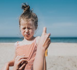 Comical image of little girl holding her breath and wincing as sun cream is applied to her face