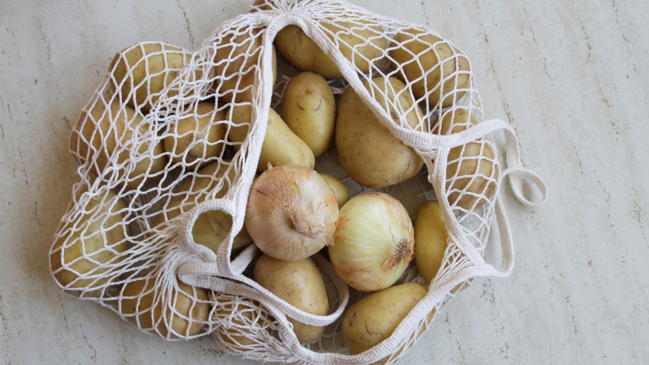 Un bolsa tirada en suelo con patatas y cebollas.