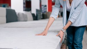 partial view of woman touching orthopedic mattress in furniture shop