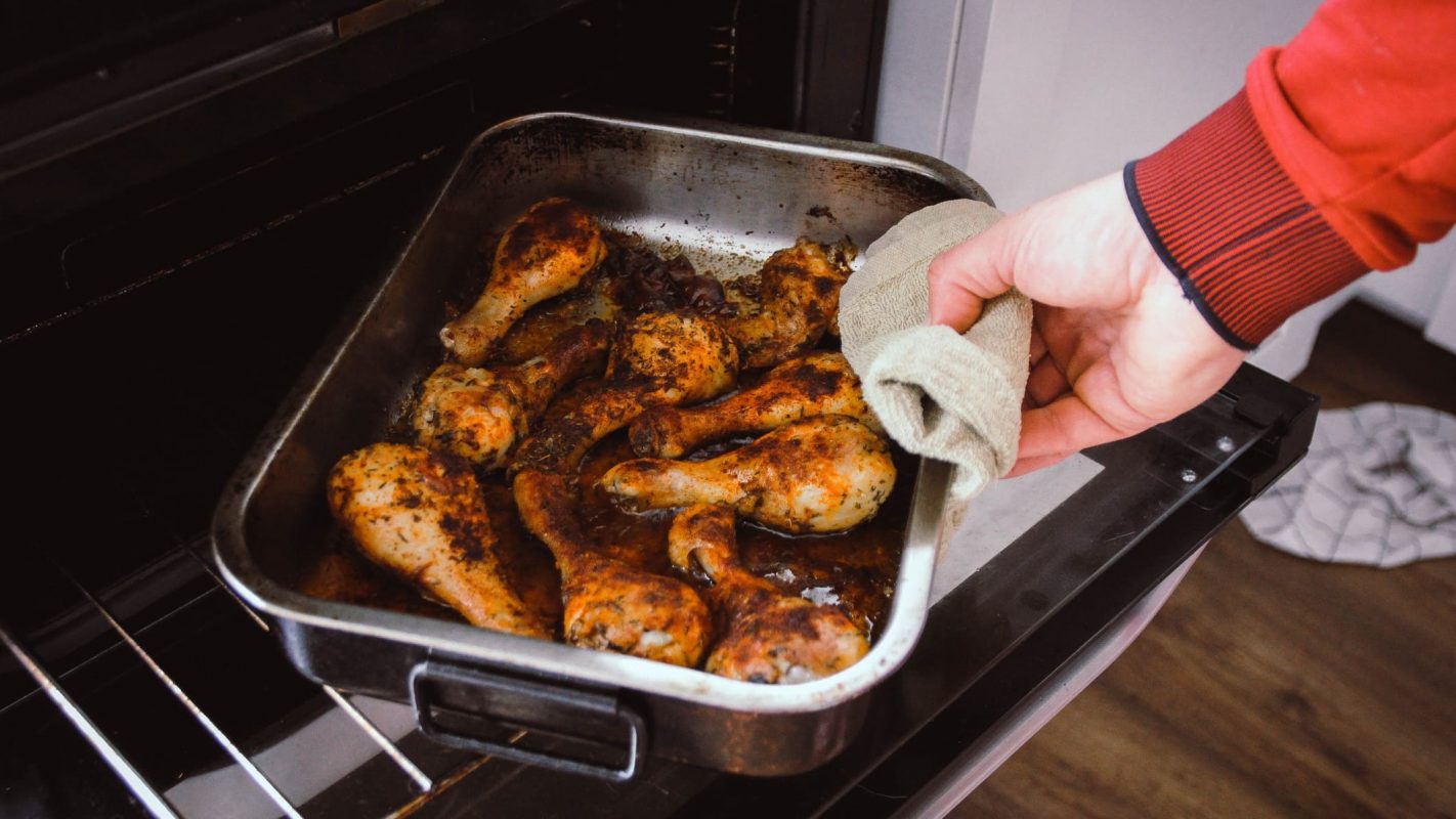 Una persona cocinando en su casa pollo al horno.