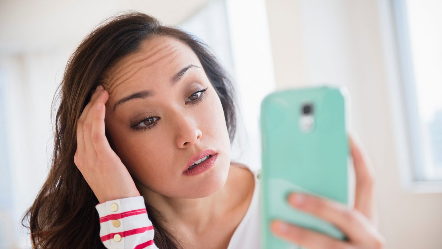 Una chica se lamenta al mirar en la pantalla del móvil una notificación que no le gusta.