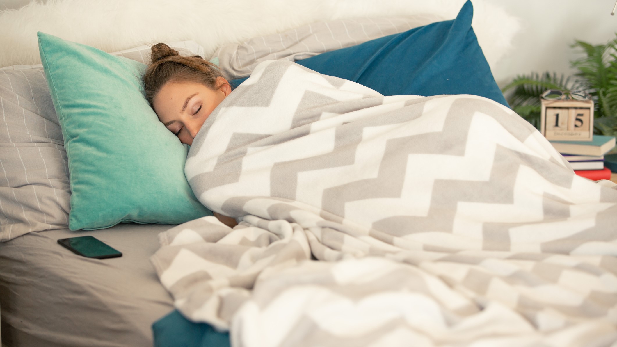 Una chica tumbada en la cama y arropada con mantas.