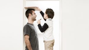 Father and son (10-11years) putting on ties, standing face to face at home, side view
