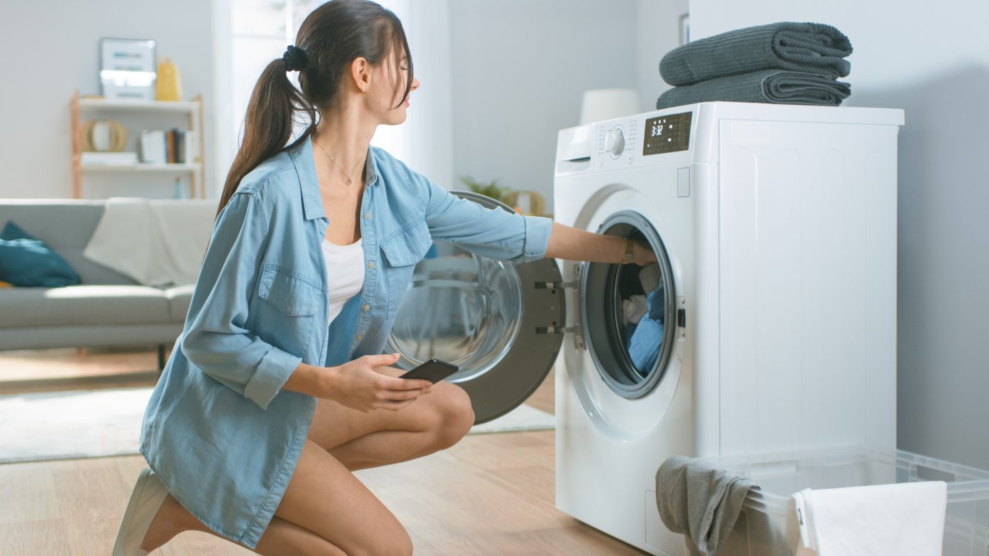 Una chica pone la lavadora con todo tipo de prendas de ropa.