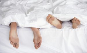 Los pies de dos personas se asoman debajo del edredón tras practicar sexo.
