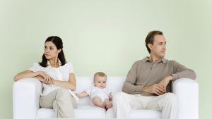 Couple sitting on couch with baby between them, both looking away