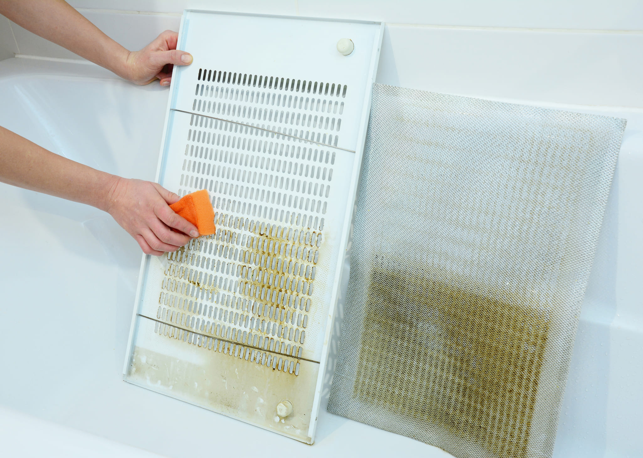 Una persona limpia los filtros de la campana extractora con una esponja en la bañera.