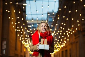 Una chica lleva una bufanda y sujeta varios regalos navideños.