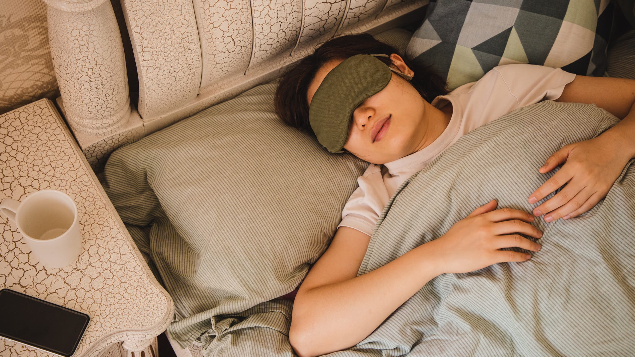 Una chica joven durmiendo en la cama con el antifaz puesto.
