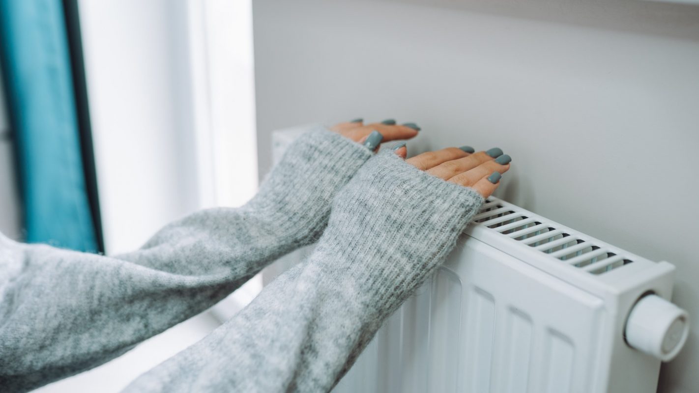 Una joven se calienta cerca del radiador de su casa.