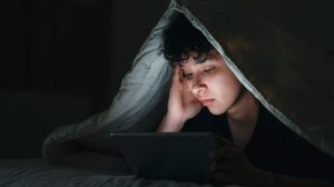 Teenage girl using smartphone in bed late at night with sad facial expression