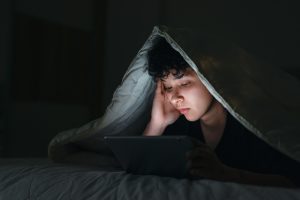 Teenage girl using smartphone in bed late at night with sad facial expression