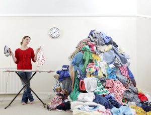 woman ironing next to very large pile of clothes