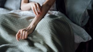 Cropped shot of young woman suffering from skin allergy, scratching her forearm with fingers