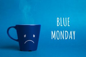 Creatividad con una taza azul con una cara triste y las palabras 'Blue Monday' sobre un fondo azul.