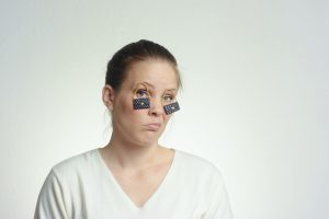 Una mujer se sujeta su párpado caído con un pequeño bolso.