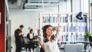 Businesswoman looking away while sitting with hands behind head at desk in office