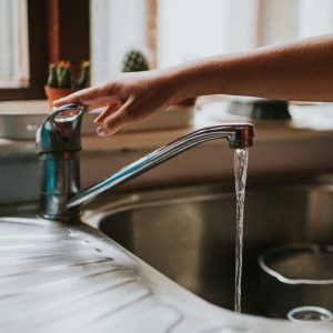 Hand turning off a Running Chrome Tap in a kitchen