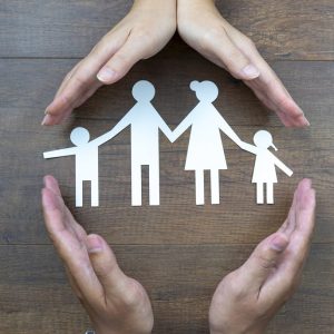 Close up of female and male hands protecting a paper chain family. Top view