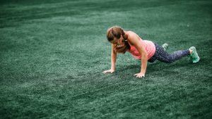 A beautiful muscular girl in leggings and a vest makes a burpee at the stadium. gym, fitness, healthy lifestyle